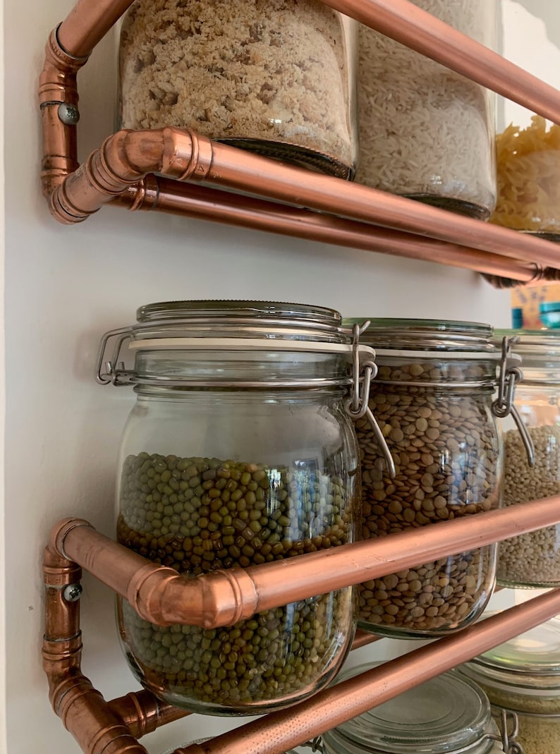 May include: Copper pipe shelving unit with glass jars filled with various dried goods, including rice, lentils, and mung beans.