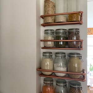 May include: A copper pipe shelving unit with glass jars filled with various dry goods, such as grains, beans, and pasta. The jars have metal lids with clips.