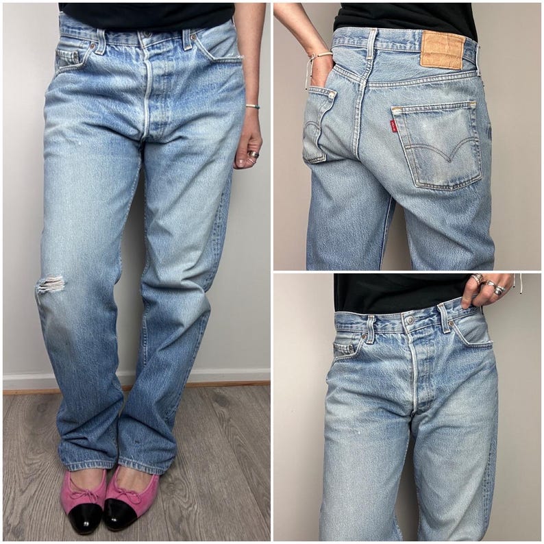 May include: Light blue denim jeans with a distressed knee. The jeans have a button fly and classic five-pocket design. A small red tag is visible on the back pocket. The jeans are worn with pink and black flats.