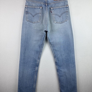 May include: Light blue denim jeans with classic five-pocket styling. The jeans feature a faded wash and a leather patch on the back. The jeans are hanging on a black hanger.