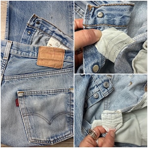 May include: Light blue denim jeans with a classic five-pocket design. Features a brown leather patch, a red tag on the back pocket, and metal button closures. The jeans show signs of wear and fading, giving them a vintage look.
