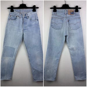 Peut inclure: Un jean en denim bleu clair avec un patch sur la jambe gauche. Le jean a une braguette à boutons et cinq poches. Les poches arrière ont un patch en cuir avec le logo Levi's.