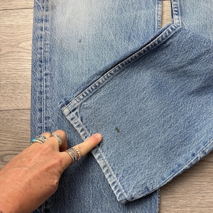 May include: Light blue denim jeans with a distressed look, featuring a ripped section near the top and a folded hem. The jeans show signs of wear and tear, with a faded wash and visible stitching details.