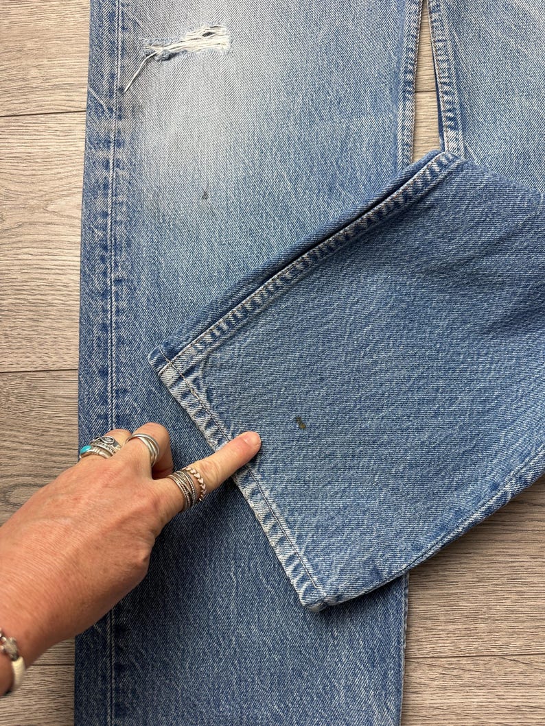 May include: Light blue denim jeans with a distressed look, featuring a ripped section near the top and a folded hem. The jeans show signs of wear and tear, with a faded wash and visible stitching details.