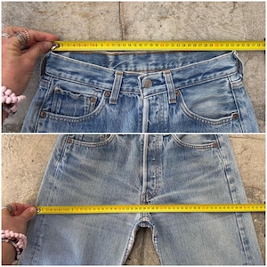 May include: Light blue denim jeans with a button fly and classic five-pocket design. A yellow measuring tape shows the waist measurement. The jeans are approximately 38 inches across the waist.