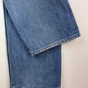 May include: Close-up of light blue denim jeans. The jeans are folded, showing the texture of the fabric and the hem of the leg. The denim has a classic, worn look.