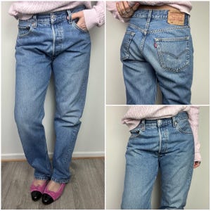 Op de afbeelding: Lichtblauwe denim jeans met een knoopsluiting en een klassiek vijf-zakken ontwerp. De jeans hebben een vervaagde wassing en een rechte pijp. Een klein rood label is zichtbaar op de achterzak. De jeans worden gedragen met roze ballerina's.