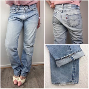 Op de afbeelding: Lichtblauwe denim jeans met een vervaagde wassing en distressed details. De jeans hebben een klassiek vijf-zakken ontwerp en een rechte pijp. De manchetten zijn opgerold, waardoor de binnennaad zichtbaar is. Een rood Levi's-label is zichtbaar op de achterzak.