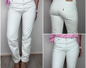 May include: High-waisted white denim jeans featuring a button fly closure, five-pocket styling, and a tan leather patch on the back waistband. The jeans have a straight-leg fit with cuffed hems, copper-toned rivets, and a small red tab on the pocket.