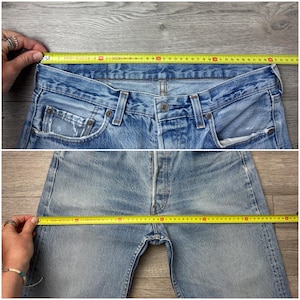 May include: Light blue denim jeans with a button fly and classic five-pocket design. The waist measures approximately 16 inches across. The jeans show signs of wear and fading, giving them a vintage look. The inseam is approximately 30 inches.
