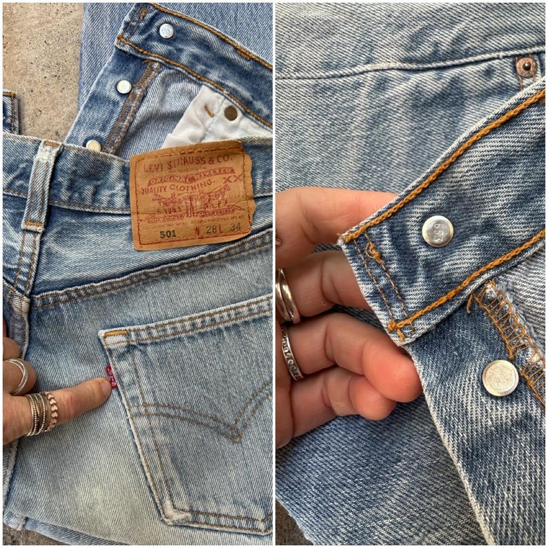 May include: Close-up of light blue denim jeans. The jeans feature a classic five-pocket design, a red tab on the back pocket, and a brown leather Levi Strauss & Co. label. The jeans have metal button closures and copper stitching.