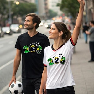 Peut inclure: Deux personnes portent des t-shirts de football noirs et blancs avec le numéro "226" en vert et jaune, et un graphisme de ballon de football. Une personne tient un ballon de football. Les chemises ont un col en V.