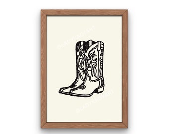 May include: A black and white illustration of a pair of cowboy boots with intricate designs on the shafts. The boots are set against a cream background and framed in a light brown wood frame.