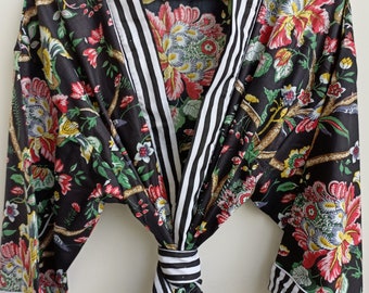 May include: Black floral print robe with white and black striped trim. The robe has a tie belt and long sleeves.