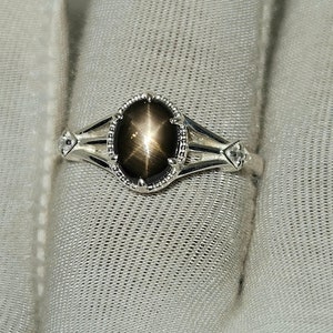 May include: A silver ring with a black star sapphire gemstone. The ring has a delicate design with a star-shaped stone in the center.