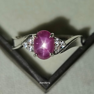 May include: A silver ring with a pink star ruby gemstone and two smaller white gemstones. The ring has a twisted band.