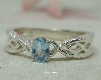 May include: A silver ring with a delicate, twisted design and a light blue oval gemstone.