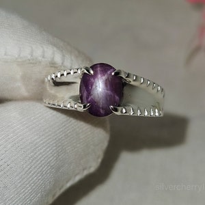 May include: A silver ring with a purple star ruby gemstone. The ring has a textured band.