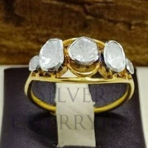 May include: A gold ring featuring five oval-shaped diamonds set in a row. The diamonds are clear and have a rough, uncut appearance.