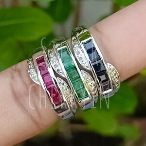 Könnte beinhalten: Vier stapelbare Ringe mit verschiedenen farbigen Edelsteinen. Die Ringe sind aus Silber und haben auf jeder Seite der Edelsteine eine Reihe kleiner Diamanten. Die Edelsteine sind smaragdgrün, rubinrot, saphiblau und ein klarer Diamant.