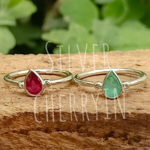 Peut inclure: Deux bagues en argent avec des pierres précieuses en forme de larme. La bague de gauche a une pierre rouge, et la bague de droite a une pierre verte.