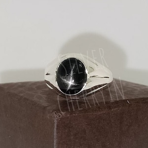 Op de afbeelding: Een zilveren ring met een zwarte edelsteen in een ovale zetting. De ring heeft een gepolijste afwerking.