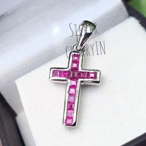 May include: A silver cross pendant with a red ruby stone inlay. The cross is set with small square-shaped rubies.