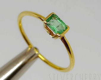 May include: A gold ring with a small, rectangular emerald gemstone. The ring is simple and elegant.