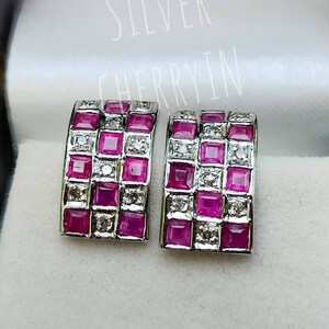 May include: A pair of silver earrings with a rectangular design. The earrings are set with pink and white square-shaped stones.