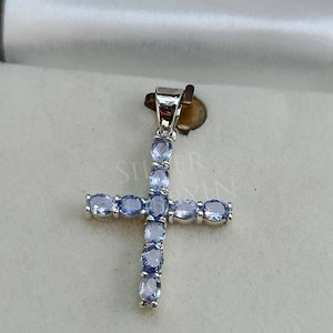 May include: A silver cross pendant with a light blue gemstone design. The cross is adorned with oval-shaped gemstones.