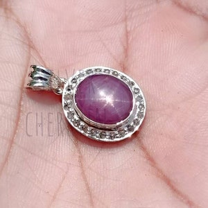 May include: A silver pendant featuring a pink star ruby gemstone surrounded by a halo of smaller white gemstones.