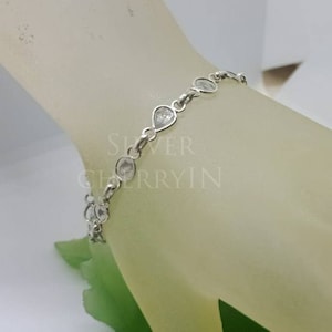 Puede incluir: Un brazalete de plata con piedras transparentes en forma de lágrima. El brazalete está en la muñeca de una modelo.