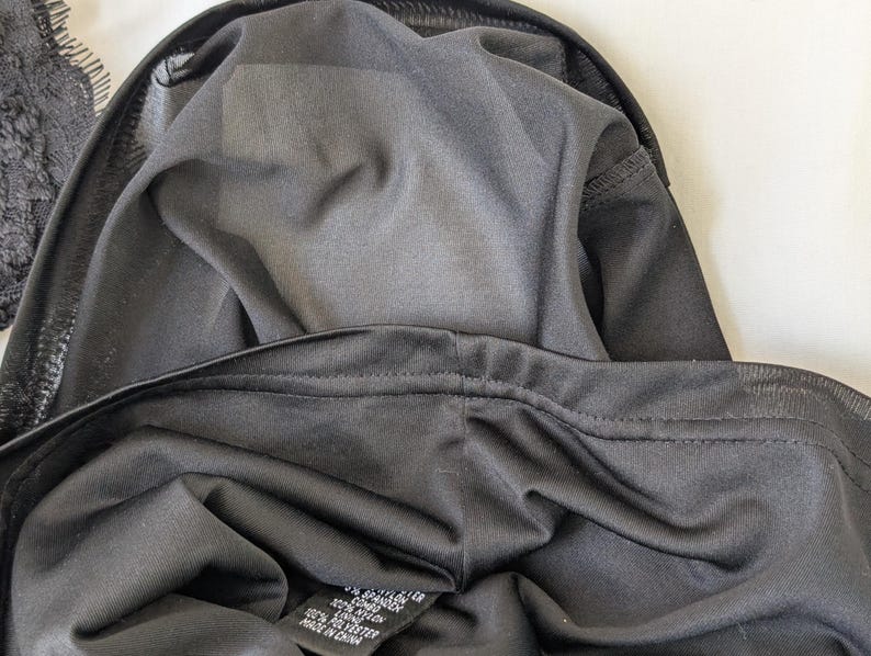 May include: Close-up of black lingerie, showcasing the fabric's texture and stitching details. The garment appears to be made of a soft, dark material, with a visible label indicating the fabric composition. The image highlights the inner lining and construction of the lingerie.