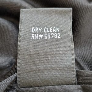 May include: Close-up of a dark gray fabric tag with the words "DRY CLEAN" and "RN #59782" printed in white. The tag is sewn onto a dark gray garment.