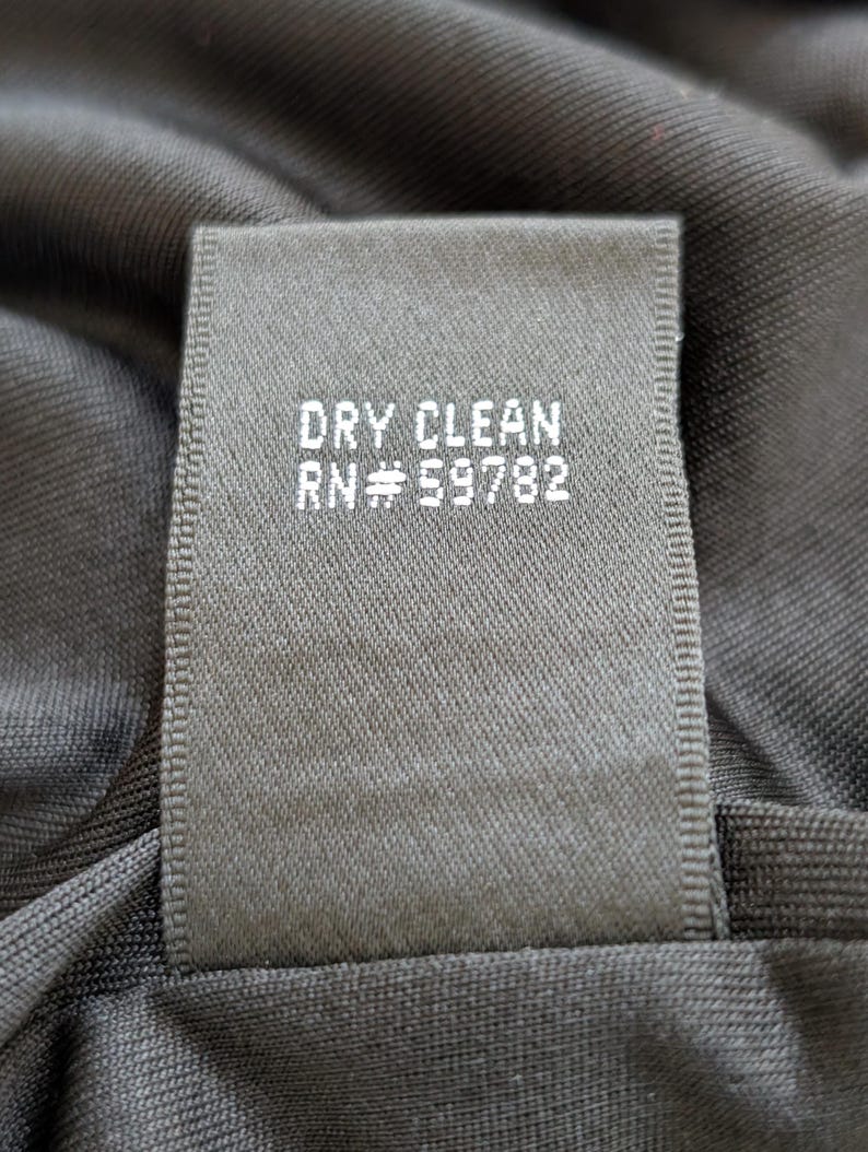 May include: Close-up of a dark gray fabric tag with the words "DRY CLEAN" and "RN #59782" printed in white. The tag is sewn onto a dark gray garment.