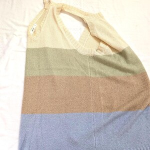 May include: A knitted top in a striped pattern of cream, olive green, tan, and light blue. The top has a halter neck design with tie straps and a V-neckline. The fabric appears soft and lightweight, suitable for warmer weather.