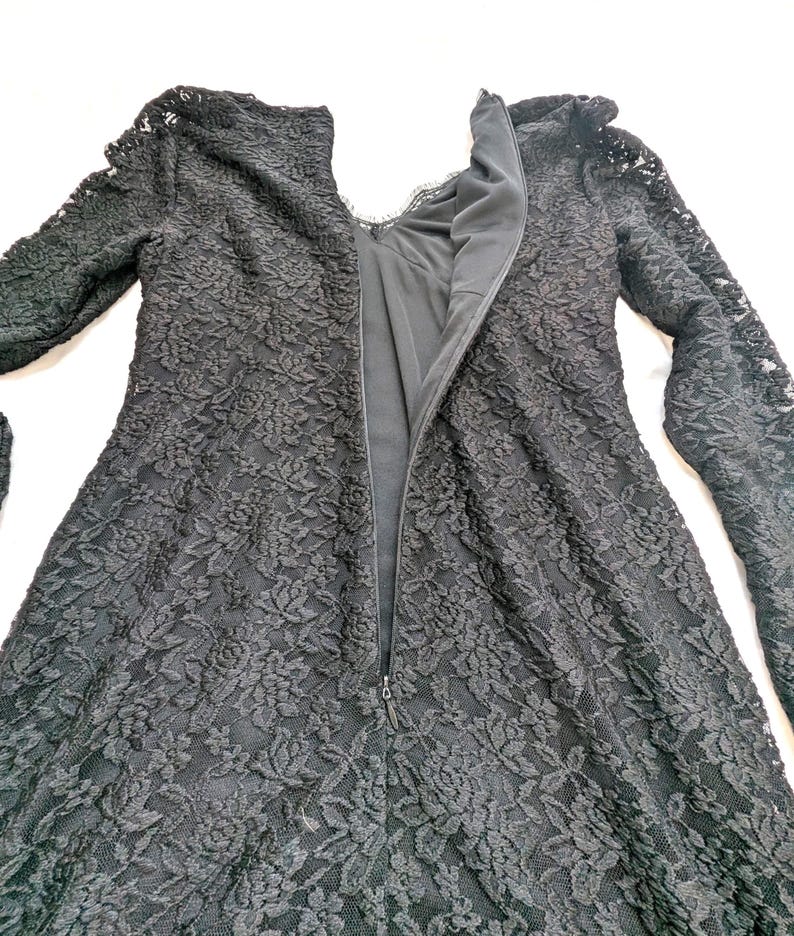 May include: A black lace dress with long sleeves and a high neckline. The dress features a floral pattern and a zipper down the back. The dress is made of a delicate lace fabric.