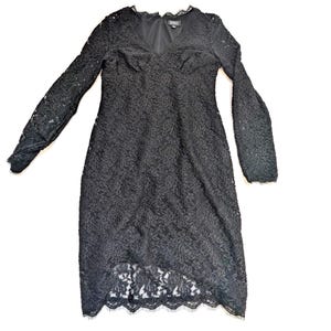 May include: Black lace dress with long sleeves and a V-neckline. The dress features a floral lace pattern and a scalloped hemline. The dress is knee-length and appears to be made of a delicate fabric.