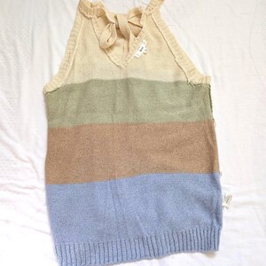 May include: A sleeveless, striped sweater in shades of beige, green, brown, and blue. The top features a V-neck with a bow detail and a ribbed hem. The sweater is made of a soft, knitted material.