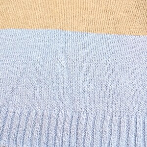 May include: Close-up of a knitted jumper with horizontal stripes. The jumper features bands of colour in light green, tan, and light blue. The knit fabric has a ribbed texture.