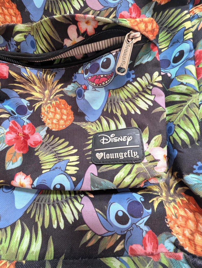 May include: A black backpack with a tropical pattern featuring the Disney character Stitch, pineapples, and flowers. The backpack has a zippered pocket and a Disney Loungefly label.