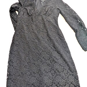 May include: A black lace dress with long sleeves and a V-neck. The dress features a floral pattern and a zipper closure. The dress is a midi length and has a delicate lace trim around the neckline.