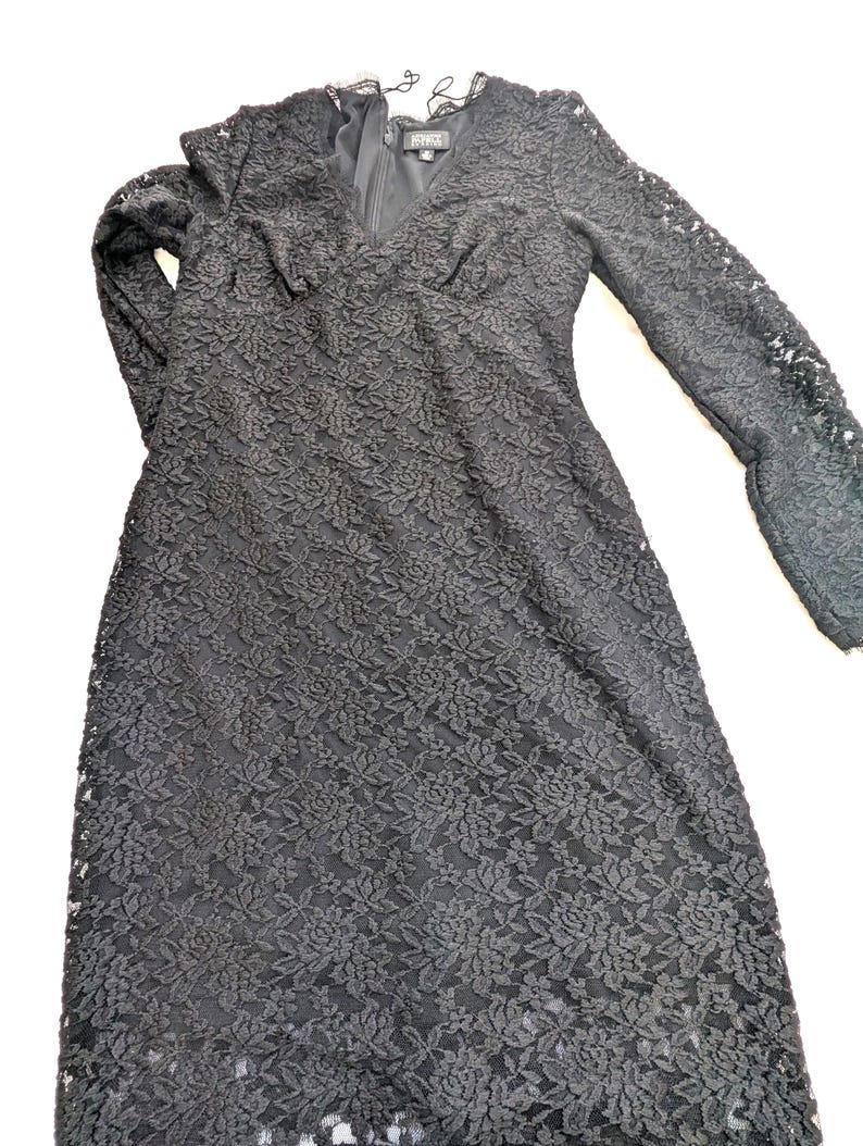 May include: A black lace dress with long sleeves and a V-neck. The dress features a floral pattern and a zipper closure. The dress is a midi length and has a delicate lace trim around the neckline.