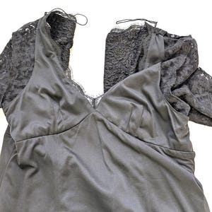 May include: A black satin dress with lace sleeves. The dress features a V-neckline and a fitted bodice. The sleeves are made of a delicate black lace. The dress is laid flat on a white surface.