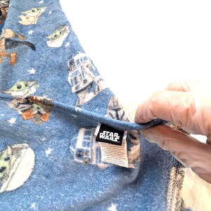 May include: Blue Star Wars fleece blanket featuring Grogu and other characters, with a white star pattern. The blanket has a tag with the Star Wars logo.