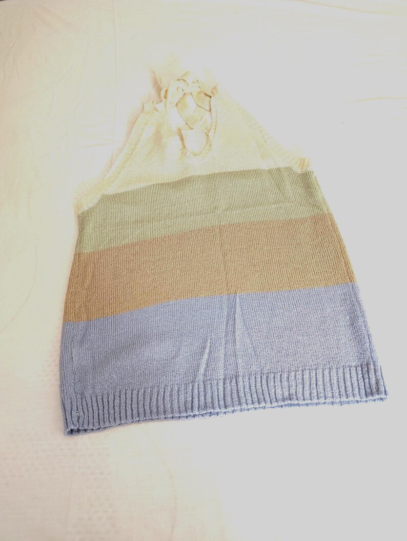 May include: A knitted top with a colour block design. The top features horizontal stripes in cream, olive green, tan, and light blue. The top has a halter neck design with cream-coloured ties.