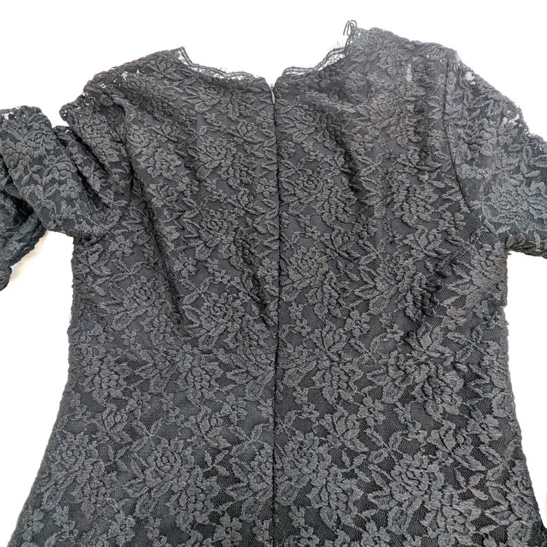 May include: Black lace dress with long sleeves. The dress features a floral pattern and a scalloped neckline. The back of the dress has a zipper closure.