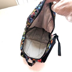 May include: A black backpack with a colorful floral and character print. The interior features a striped lining. The backpack has a zipper closure and black straps.