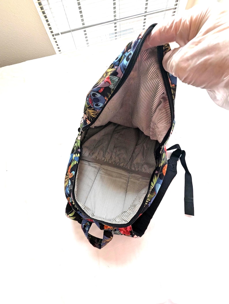 May include: A black backpack with a colorful floral and character print. The interior features a striped lining. The backpack has a zipper closure and black straps.