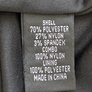 May include: A black fabric tag with white text detailing the material composition of a garment. The tag lists "SHELL" with 70% polyester, 27% nylon, and 3% spandex. It also includes "COMBO" and "LINING" details, and states "MADE IN CHINA."